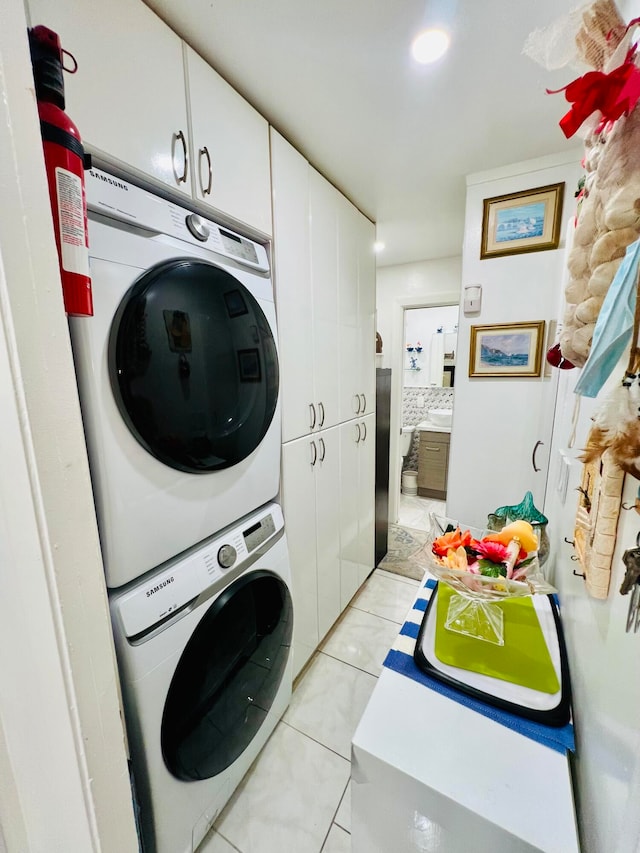 clothes washing area featuring stacked washer and clothes dryer, cabinets, and light tile flooring