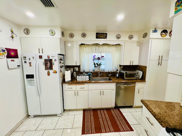 kitchen with white cabinets, dark stone counters, stainless steel dishwasher, and white refrigerator with ice dispenser