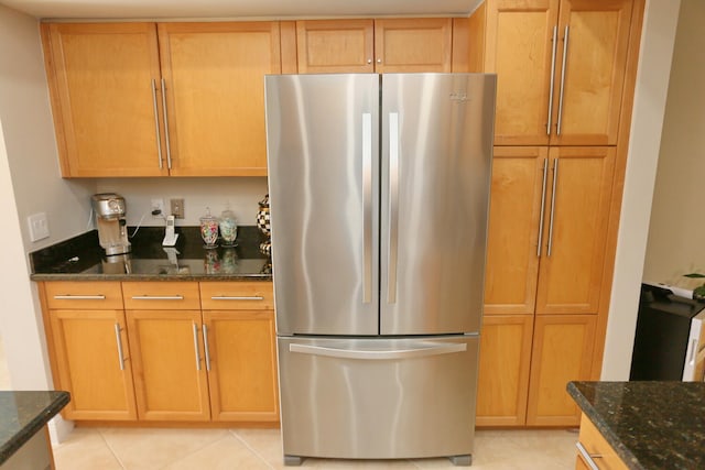 kitchen with stainless steel refrigerator, light tile flooring, and dark stone countertops