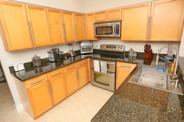 kitchen featuring stainless steel appliances, light tile floors, dark stone countertops, and sink