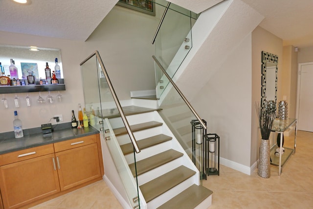 staircase featuring a textured ceiling, light tile flooring, and bar