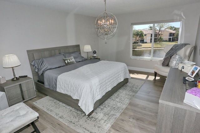 bedroom featuring a water view, light hardwood / wood-style floors, and a notable chandelier