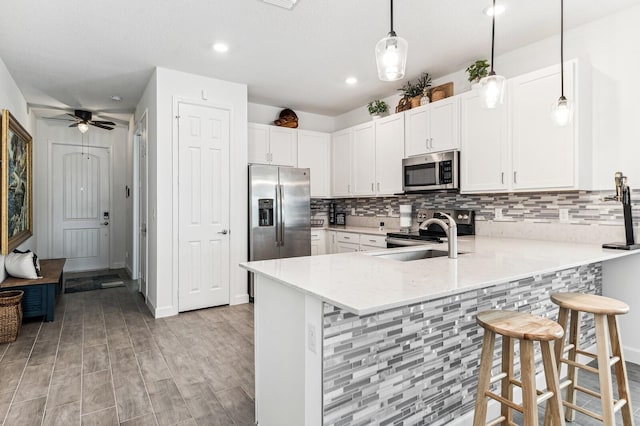 kitchen featuring kitchen peninsula, ceiling fan, a breakfast bar, stainless steel appliances, and decorative light fixtures