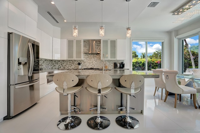 kitchen with decorative backsplash, wall chimney range hood, stainless steel refrigerator with ice dispenser, white cabinetry, and light stone counters