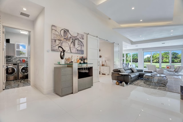 tiled living room with independent washer and dryer, a tray ceiling, and bar area