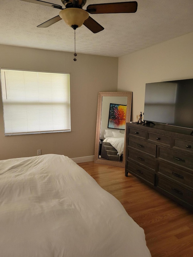 bedroom with a textured ceiling, wood-type flooring, and ceiling fan