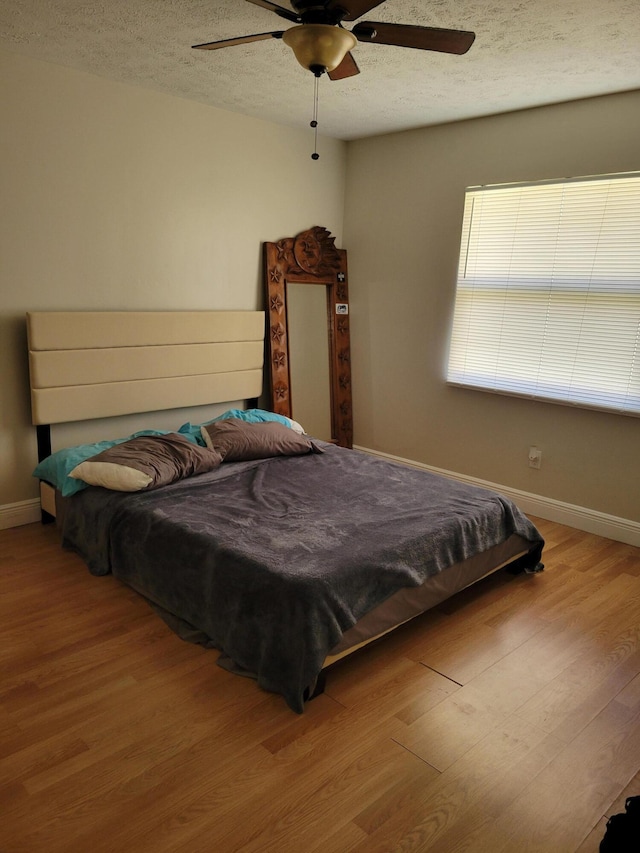 bedroom with ceiling fan, light hardwood / wood-style flooring, and a textured ceiling