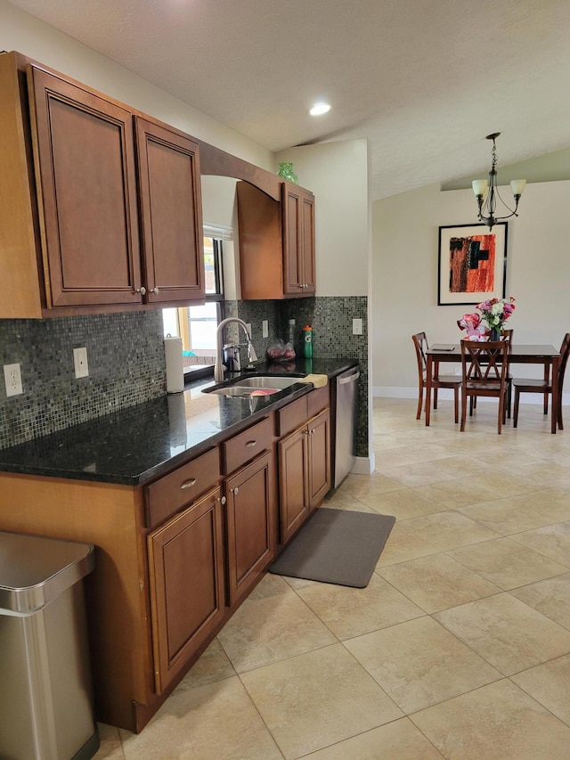 kitchen with stainless steel dishwasher, a notable chandelier, dark stone counters, tasteful backsplash, and sink