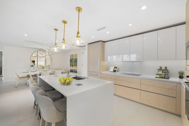 kitchen with light brown cabinets, light tile floors, a center island with sink, hanging light fixtures, and sink