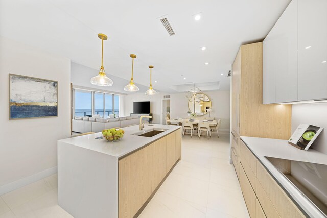 kitchen with light brown cabinets, light tile floors, white cabinets, a center island with sink, and pendant lighting