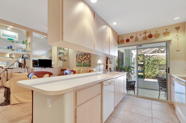 kitchen with kitchen peninsula, white dishwasher, sink, and light tile flooring