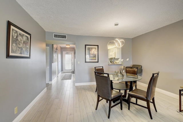 dining area with an inviting chandelier, a textured ceiling, and light wood-type flooring