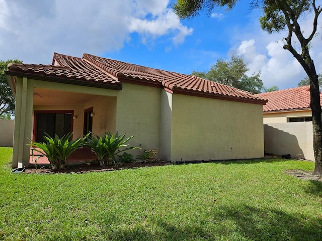 view of property exterior with a tiled roof, a lawn, fence, and stucco siding