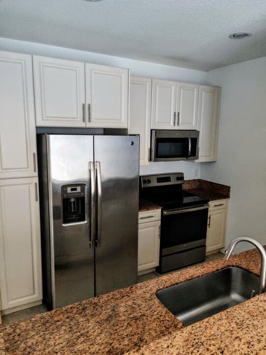 kitchen featuring stainless steel appliances, white cabinets, and dark stone counters