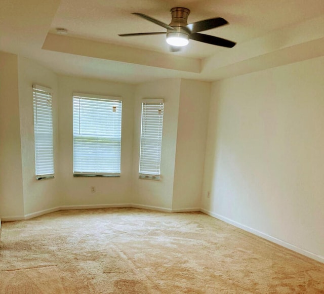 carpeted empty room with a raised ceiling and ceiling fan