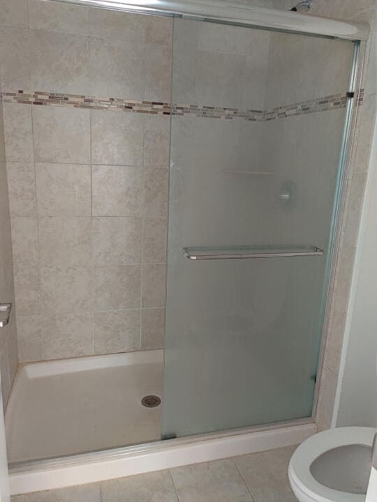 bathroom with an enclosed shower, tile floors, and toilet