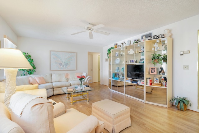 living room featuring light hardwood / wood-style floors, ceiling fan, and a textured ceiling