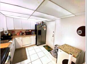 kitchen with a drop ceiling, white cabinetry, stainless steel fridge, range, and light tile floors