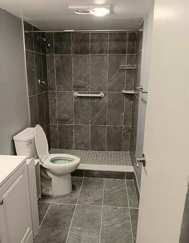 bathroom featuring tiled shower, toilet, tile flooring, and vanity