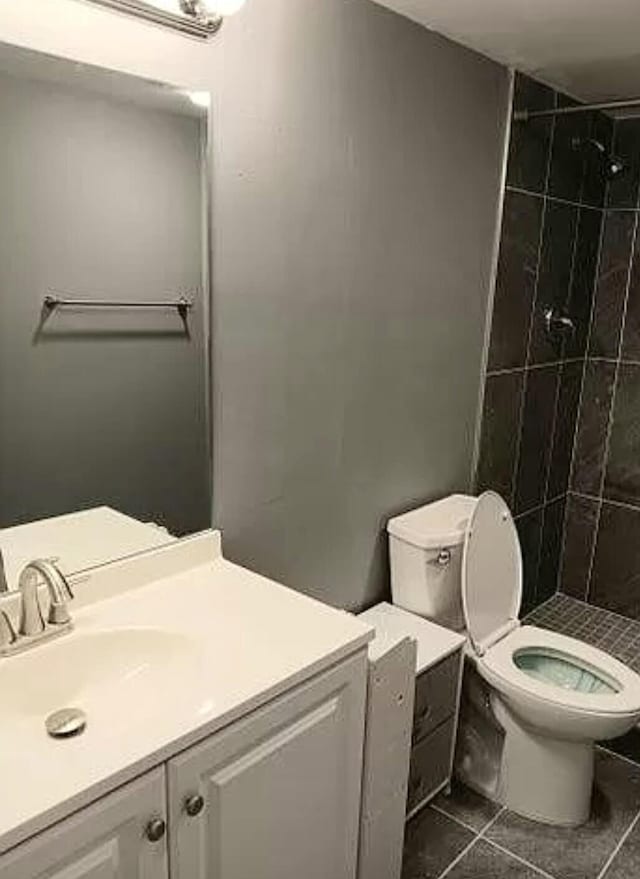 bathroom featuring tile flooring, tiled shower, vanity, and toilet