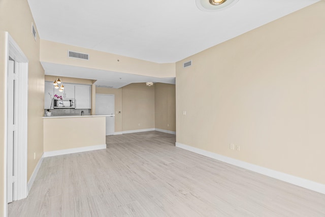 unfurnished living room with an inviting chandelier and light hardwood / wood-style floors