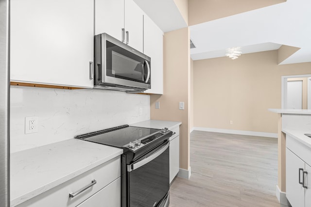 kitchen featuring a notable chandelier, light stone countertops, range with electric cooktop, light hardwood / wood-style flooring, and white cabinetry