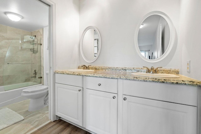 full bathroom featuring toilet, double sink, enclosed tub / shower combo, large vanity, and hardwood / wood-style flooring