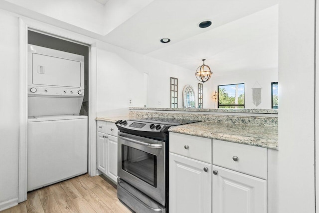 kitchen with stainless steel electric range, light stone counters, light hardwood / wood-style floors, stacked washing maching and dryer, and white cabinetry