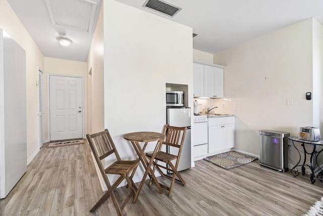 interior space featuring light hardwood / wood-style floors, tasteful backsplash, fridge, white cabinets, and sink