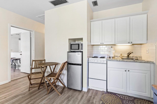 kitchen with light hardwood / wood-style floors, stainless steel appliances, tasteful backsplash, white cabinetry, and light stone counters