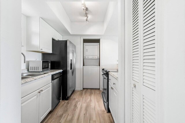 kitchen featuring stainless steel appliances, stacked washer / drying machine, light hardwood / wood-style flooring, white cabinets, and track lighting