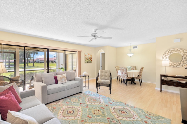 living room with ceiling fan, light wood-type flooring, and a textured ceiling