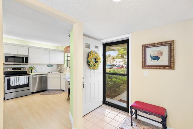 kitchen featuring stainless steel appliances, light hardwood / wood-style floors, a textured ceiling, sink, and white cabinets