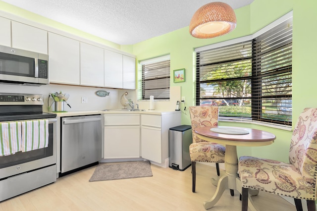 kitchen featuring sink, appliances with stainless steel finishes, light hardwood / wood-style floors, a textured ceiling, and white cabinetry