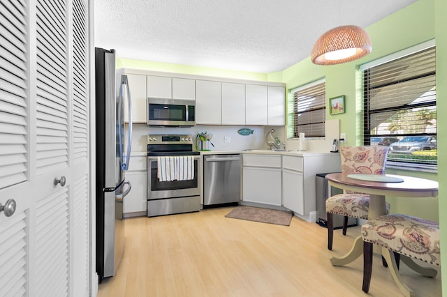 kitchen featuring decorative light fixtures, appliances with stainless steel finishes, light hardwood / wood-style floors, white cabinetry, and a textured ceiling