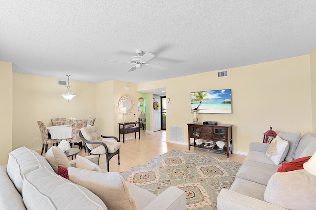 living room featuring ceiling fan, light hardwood / wood-style floors, and a textured ceiling