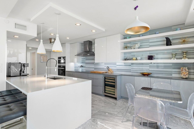 kitchen with white cabinetry, wall chimney exhaust hood, hanging light fixtures, wine cooler, and a kitchen bar