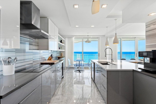 kitchen with a water view, sink, wall chimney exhaust hood, decorative light fixtures, and white cabinetry