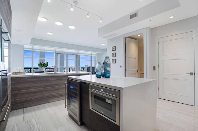 kitchen with a kitchen island, a healthy amount of sunlight, wine cooler, and stainless steel oven