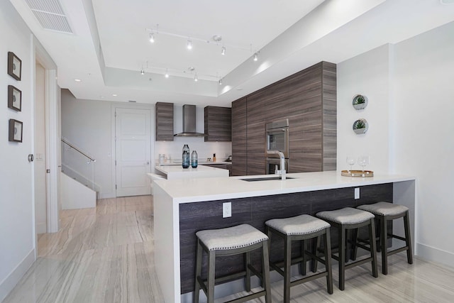 kitchen with a breakfast bar area, light hardwood / wood-style flooring, kitchen peninsula, and wall chimney range hood