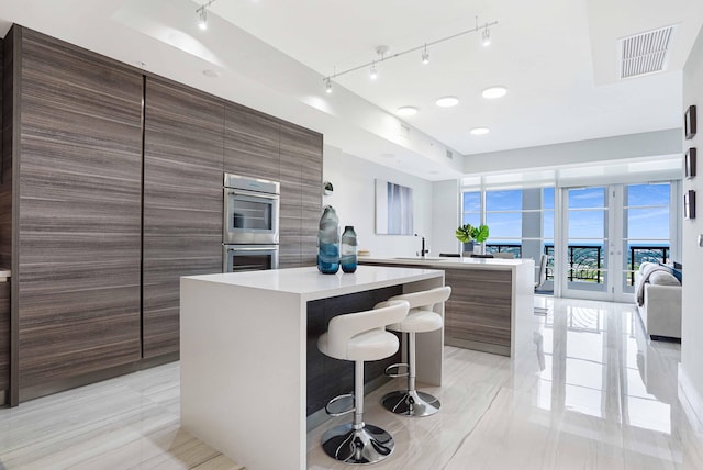 kitchen featuring rail lighting, a breakfast bar area, sink, double oven, and a center island