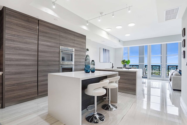 kitchen with sink, a kitchen island, track lighting, double oven, and a kitchen breakfast bar