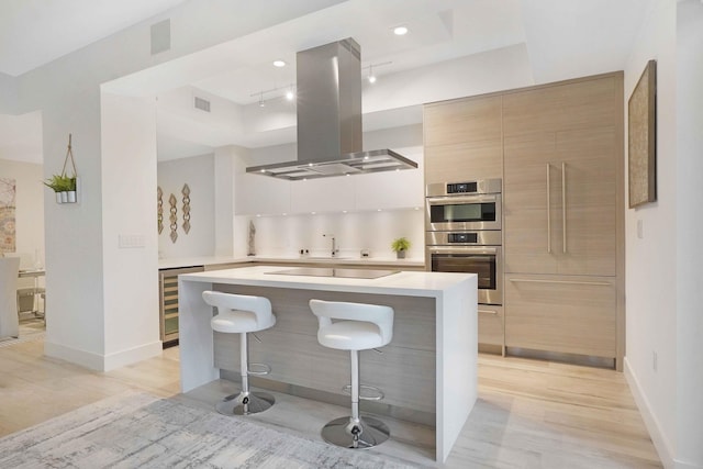 kitchen featuring wine cooler, island range hood, a breakfast bar, stainless steel double oven, and light hardwood / wood-style floors