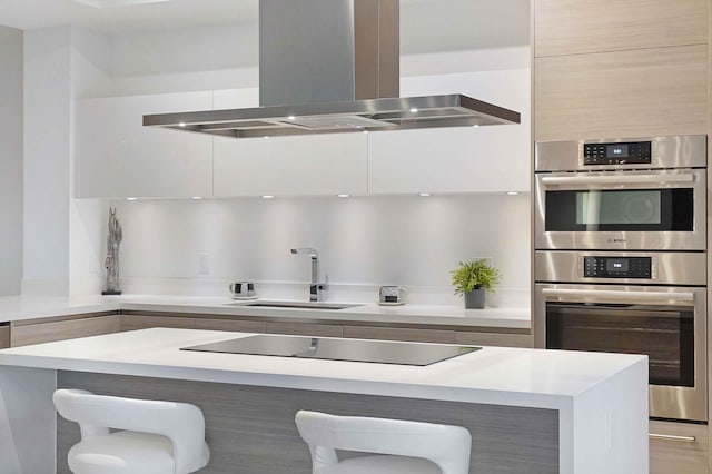 kitchen featuring a breakfast bar area, stainless steel double oven, black electric cooktop, sink, and island range hood