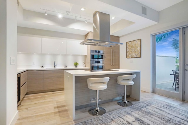 kitchen with a kitchen breakfast bar, island exhaust hood, a kitchen island, and white cabinetry