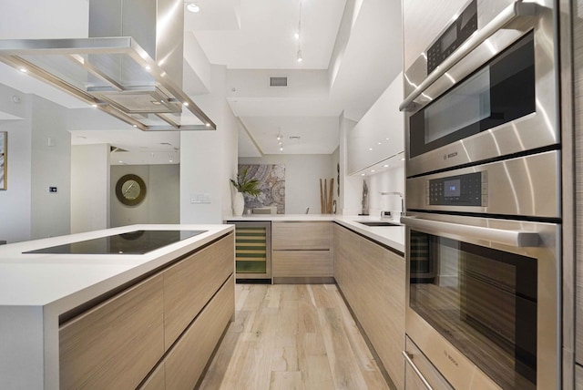 kitchen featuring light brown cabinets, light hardwood / wood-style flooring, island exhaust hood, wine cooler, and black electric stovetop