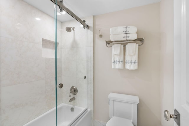 bathroom featuring toilet and shower / bath combination with glass door