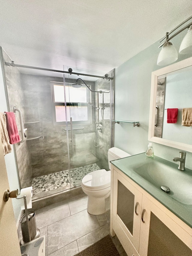 bathroom featuring a shower with door, tile flooring, large vanity, and toilet