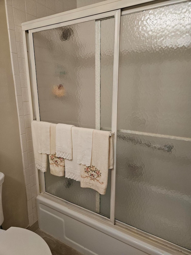 bathroom featuring enclosed tub / shower combo and toilet