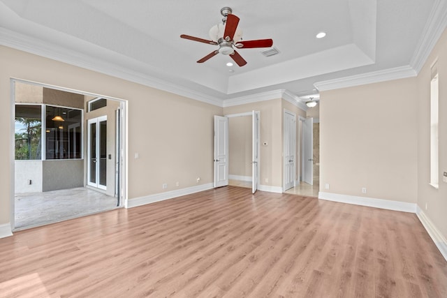 empty room with crown molding, a tray ceiling, ceiling fan, and light wood-type flooring